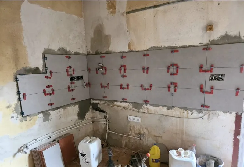 Pared a medio alicatar con crucetas niveladoras rojas entre los azulejos