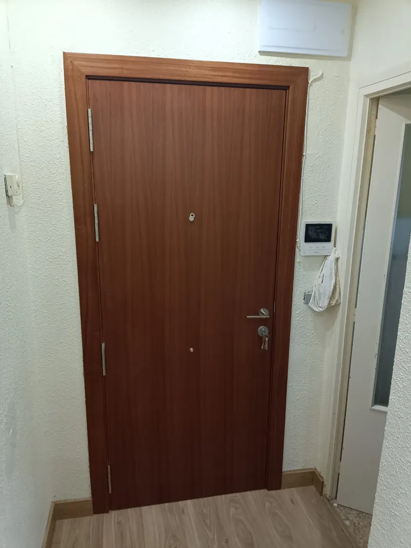Puerta de entrada de vivienda color caoba montada, con videoportero al lado y suelo laminado