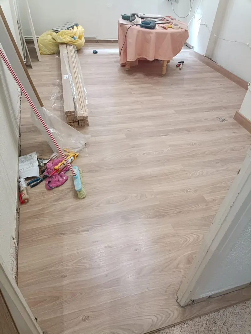 Salón con el suelo laminado recién colocado y los rodapiés todavía apilados