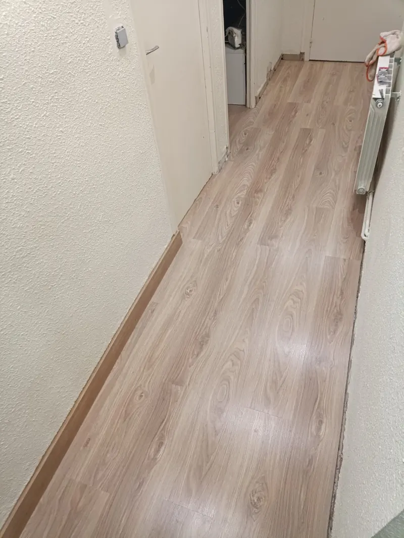 Pasillo con suelo laminado colocado; el rodapié está puesto en una de las paredes y falta todavía en el tramo junto al radiador