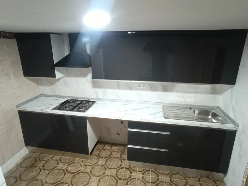 Cocina en línea negro brillo con encimera efecto mármol, campana negra, placa de gas y suelo hidráulico antiguo
