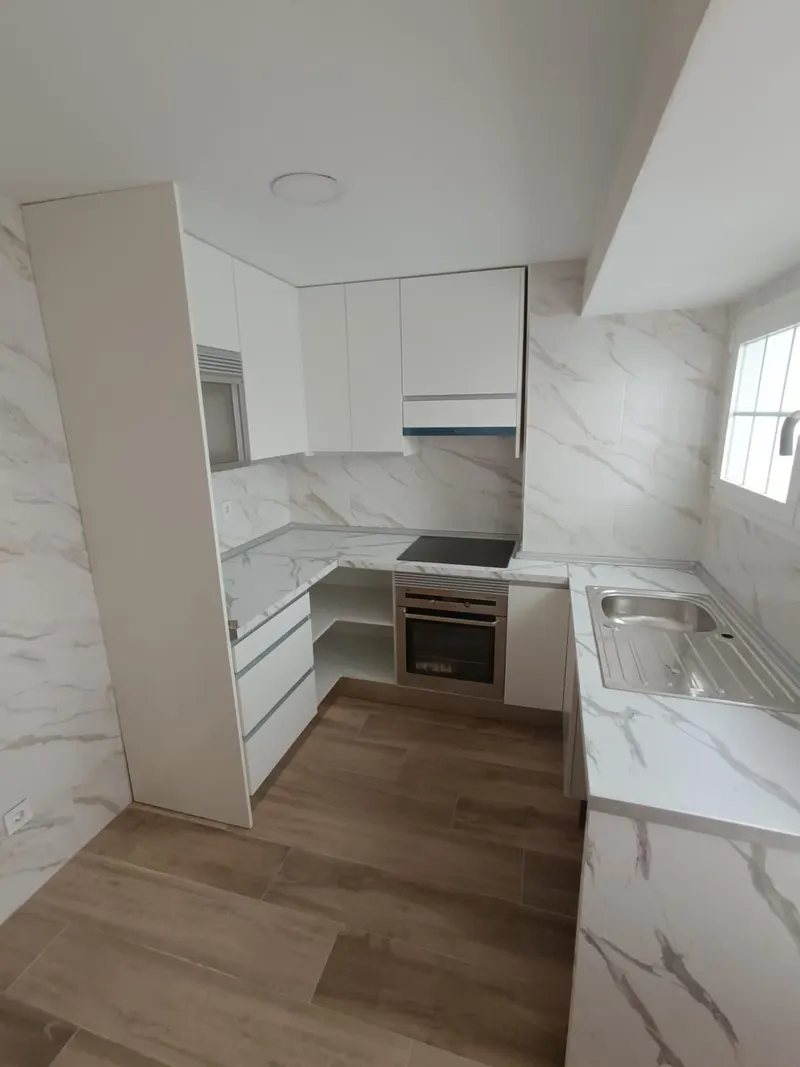 Cocina blanca en U con alicatado y encimera efecto mármol, horno y vitrocerámica, y suelo porcelánico imitación madera