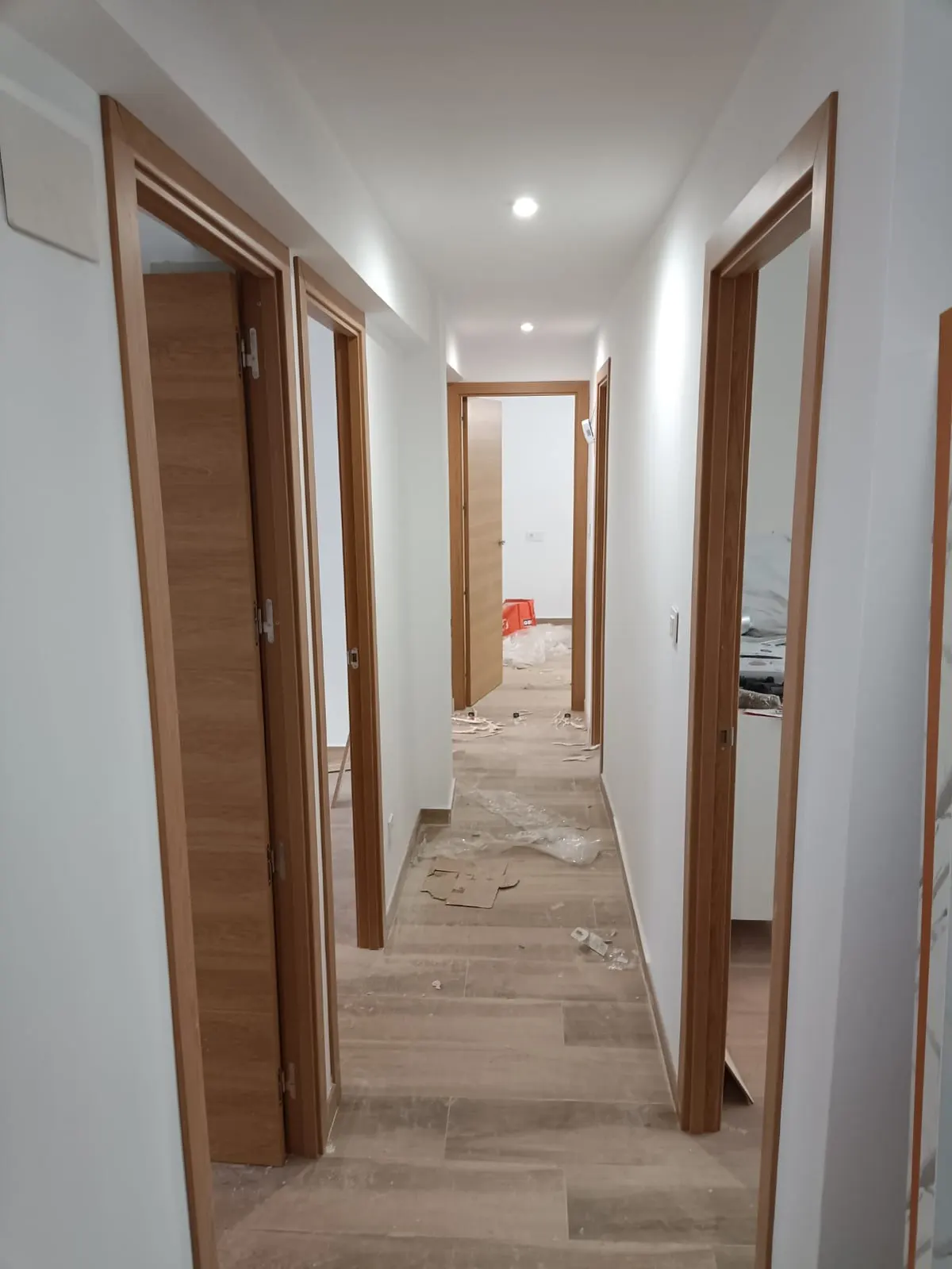 Pasillo con cuatro puertas de roble montadas, suelo porcelánico y algunos restos de obra