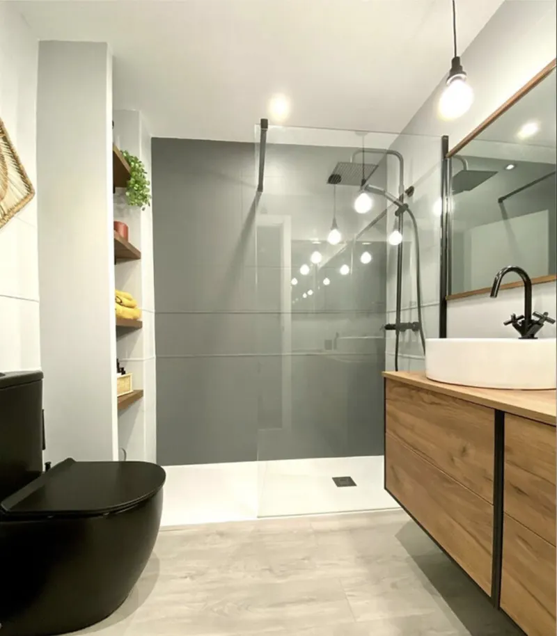 Baño con ducha de obra en gran formato gris, grifería negra, mueble de madera con lavabo y sanitario negro